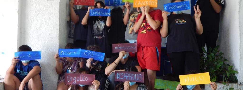 Fotografía. Un grupo de niños, niñas y adolescentes muestras unos pequeños carteles de colores con diferentes palabras- Por ejemplo: desarrollo, cambios, orgullo, progreso, crecer.