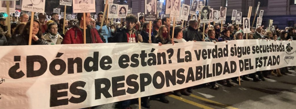 Fotografía. Marcha del Silencio. Un grupo de personas manifestándose en la calle con fotos de detenidos desaparecidos y con una pancarta que dice "¿Dónde están? La verdad sigue secuestrada, es responsabilidad del Estado"
