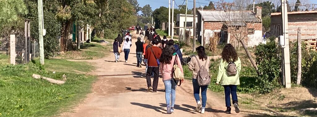 Fotografía. Exterior. Un grupo de estudiantes caminan en una calle de tierra.